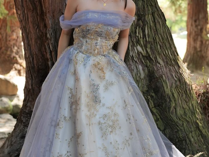 Besondere Stoffe und eine große Auswahl an Faden in verschiedenen Farben beim Nähstudio Davud in Frankfurt - Ihre Änderungsschneiderei Elegantes, bodenlanges Kleid mit lila und goldenen Akzenten, vor einem Baum getragen.